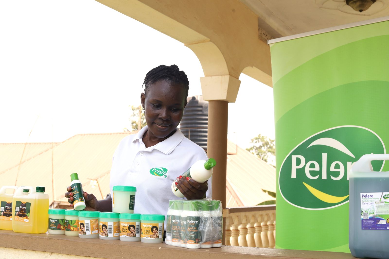Sandra Letio holding a Pelere leave-in treatment bottle beside Pelere shea jelly, hair pomade, shampoo and detergent products